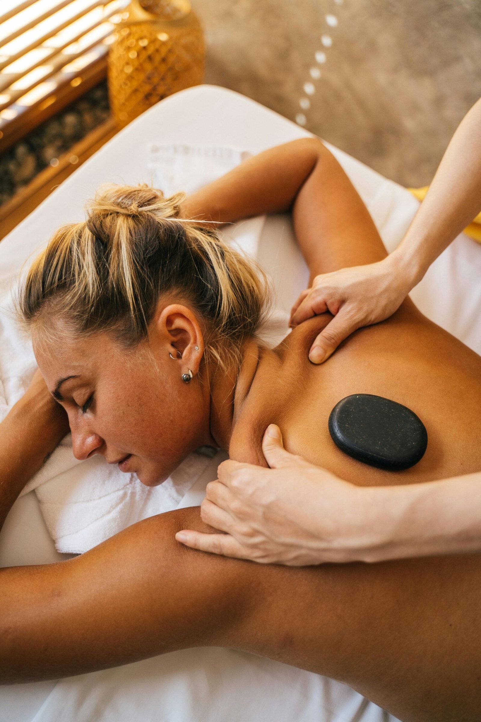 Woman enjoying a hot stone massage at a spa, promoting relaxation and pampering.